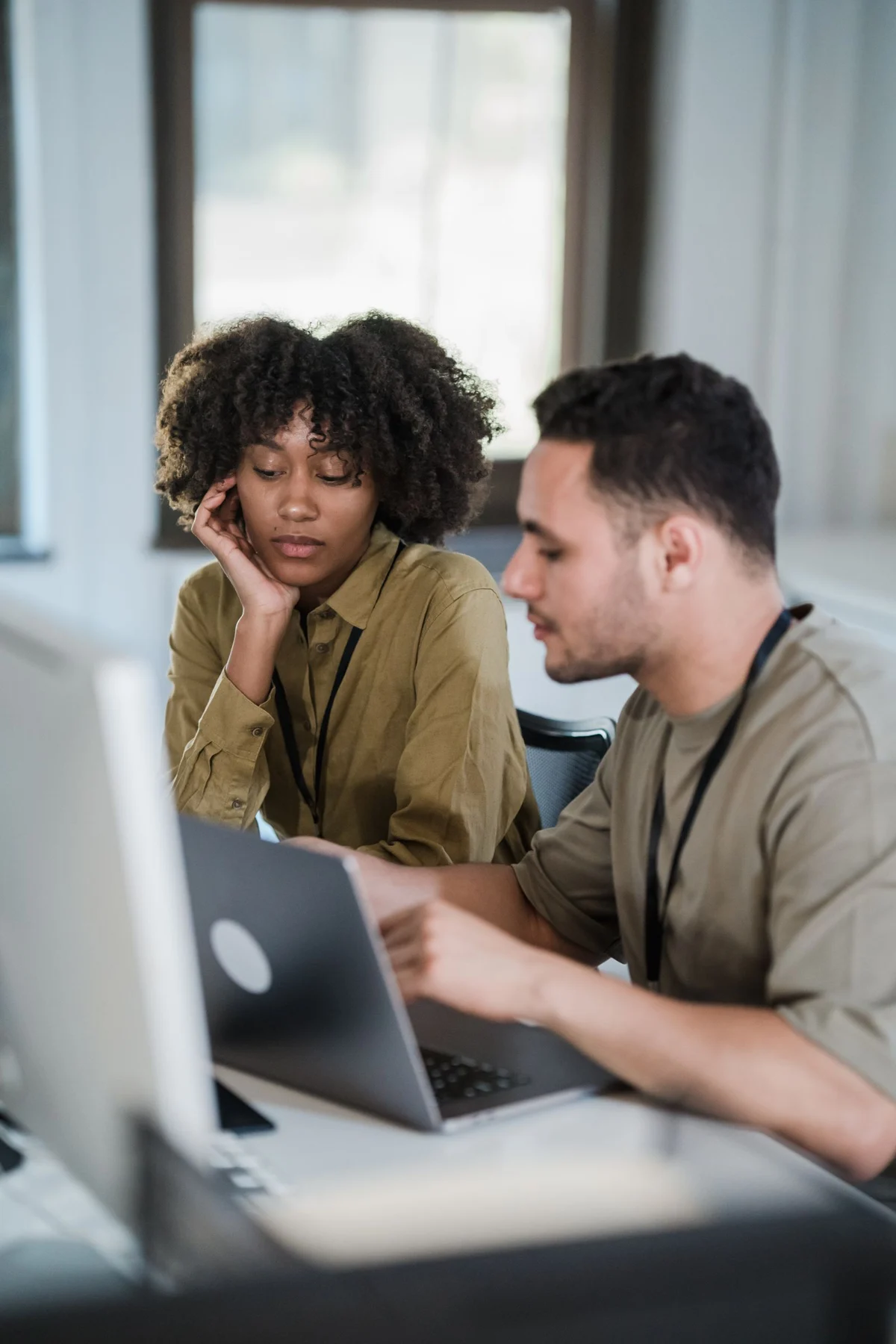 Two colleagues working together at a laptop and desktop monitor in an office